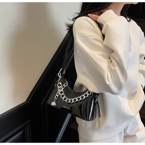 Detail of black patent leather shoulder bag with silver chain and brand logo on model