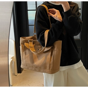 Detail of khaki canvas tote bag featuring large front buckle pocket and side pocket