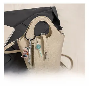 Detail of cream lychee texture leather bucket bag with cute bear and candy charms