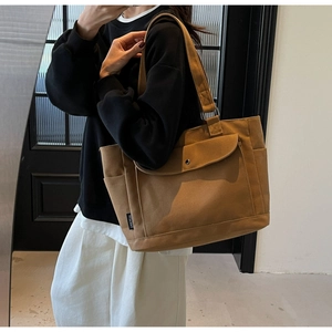 Detail of a large brown canvas tote bag featuring a front flap pocket and a side pocket