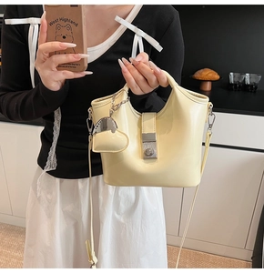 Detail of beige bucket bag with heart pendant, metal clasp and detachable strap