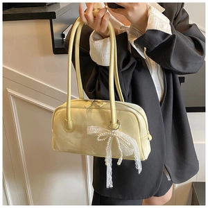 Detail of a creamy yellow shoulder bag with pearl lace bow charm on long leather handles
