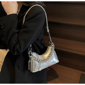 Detail of silver metallic crescent bag with thick chain strap worn by a model in black suit