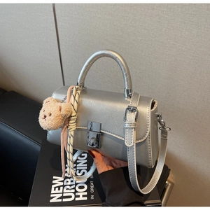 Close-up of a silver metallic crossbody bag featuring a square twist lock and a cute bear charm