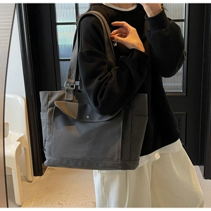 Detail of dark grey canvas tote bag showing front flap pocket with metal snap button