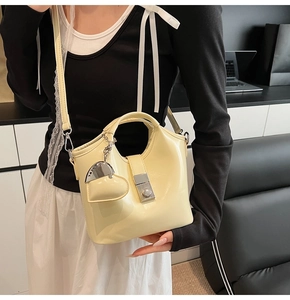 Detail of cream bucket bag with silver buckle and heart charm on a crossbody strap