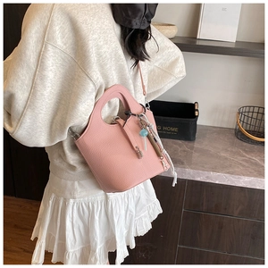 Pink bucket bag with lychee grain texture and adjustable shoulder strap shown in a room
