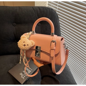 Close-up of a pink glossy handbag with a silver snap button and a plush bear pendant