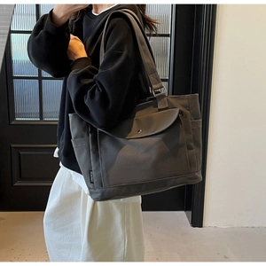 Detail of dark grey canvas tote bag with front pocket and brand label shown on shoulder