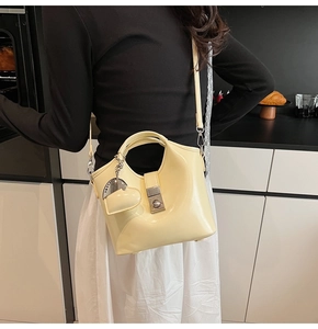 Detail of creamy yellow bucket bag featuring a glossy finish and a heart charm pendant