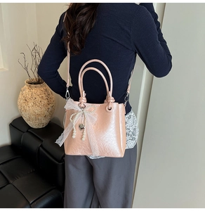 Détail du sac seau en cuir rose avec nœud en dentelle et breloque perle sur un canapé