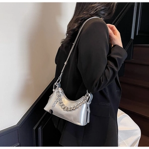 Detail of silver metallic underarm bag with thick chain strap worn by a model