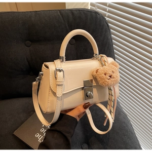 Detail of cream white faux leather handbag with silver clasp and plush bear charm decoration