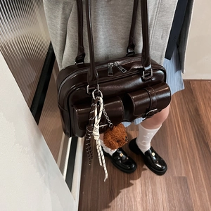 Detail of dark brown PU leather Boston bag with pocket buckles and plush bear charm