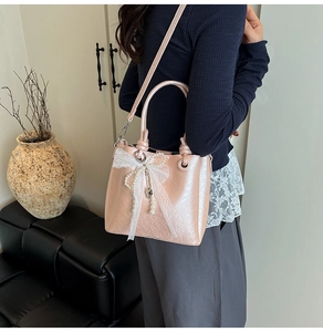 Détail d'un sac seau rose avec nœud en dentelle, perle et texture PU brillante