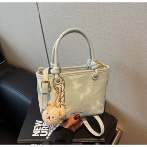 Detail of light blue faux leather bucket bag with plush bear charm and woven lanyard