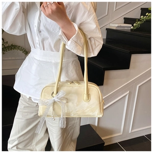 Detail of a creamy yellow glossy handbag with lace bow and pearl charm worn by a model