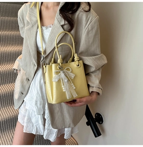 Détail du sac seau jaune avec nœud en dentelle et perles porté par un mannequin en veste