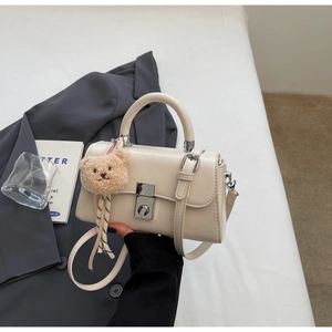 Detail of cream white leather handbag with silver twist lock and plush bear charm