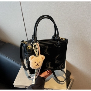 Detail of black glossy bucket bag with knot handle and plush bear charm on white box