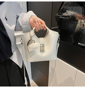 Close-up of white bucket bag featuring silver twist lock and heart-shaped pendant detail