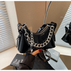 Detail of black patent leather baguette bag with thick silver chain and metal charm