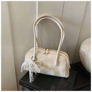 Close-up of cream leather pillow bag with elegant lace bow and pearl charm on a book
