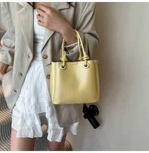 Détail d'un sac seau jaune clair avec poignée nouée et accents de bague en métal argenté