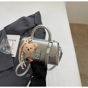 Detail of silver leather handbag with flap closure and cute beige plush bear pendant
