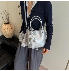 Détail du sac seau métallisé argenté avec nœud en dentelle blanche et pendentif perle