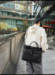 Water-resistant black travel bag detail showing front pockets and shoulder strap