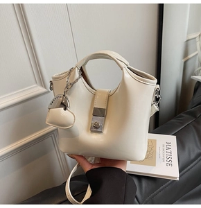 Detailed shot of cream bucket bag with silver buckle, heart charm and adjustable strap