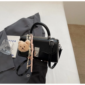 Detail of a black glossy PU leather handbag with silver lock and plush bear pendant