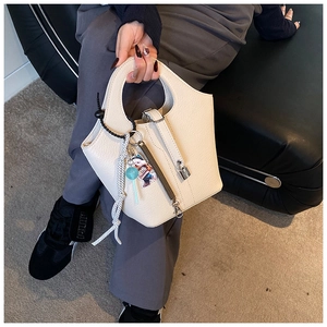 Detail of a beige pebbled leather bucket bag featuring a silver padlock and cute charms