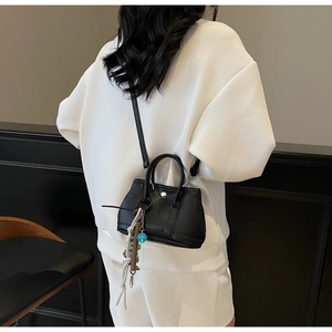 Detailansicht der schwarzen Eimertasche aus genarbtem Leder mit Anhängern und Schnalle