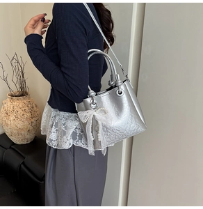 Détail du sac seau argenté avec texture métallisée, nœud en dentelle et breloque perle