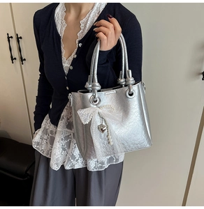 Détail du sac seau argenté avec nœud en dentelle blanche et pendentif cœur en perles