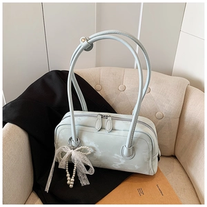 Detail of light blue boston bag with white lace bow and pearl charm on a beige sofa