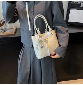 Détail du sac seau crème avec nœud en dentelle, perles et pendentif cœur argenté