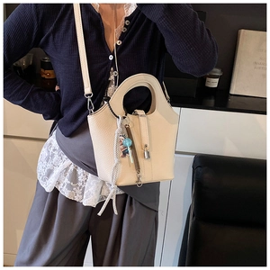 Detail of a creamy white bucket bag featuring pebble leather texture and a cute bear charm