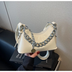 Detail of cream patent leather half-moon bag with chunky silver chain and zip closure