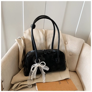 Chic black leather shoulder bag with lace bow pendant displayed on a cozy sofa chair