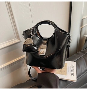 Detail of glossy black bucket bag with silver heart charm and metal chain strap