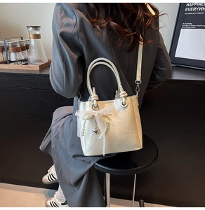 Détail du sac seau crème avec nœud en dentelle et pendentif perle en forme de cœur