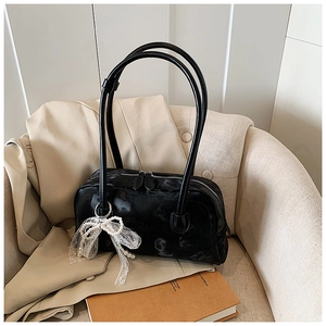 Detail of black glossy pillow bag featuring pearl lace bow and double zipper closure