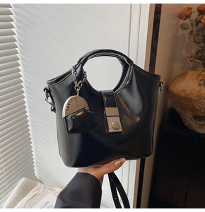 Detail view of black glossy leather bucket bag with metallic buckle and heart pendant