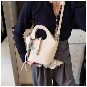Detail of off-white lychee pattern leather bucket bag with metal lock and blue charm