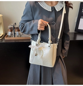 Détail du sac seau blanc avec nœud en dentelle, perles et pendentif en forme de cœur