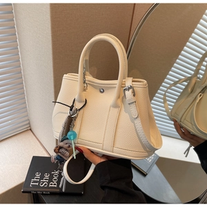 Detailansicht der cremeweißen Beuteltasche aus Leder mit zwei Anhängern und Schultergurt