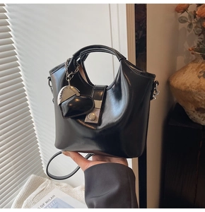 Detail showing high-gloss black leather bucket bag with silver heart charm and metal clasp